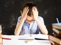 Chłopiec z rękami na głowie, otoczony książkami, zmaga się z nauką. Czy to dysleksja, co to za trudność?