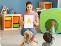 Nauczycielka prezentuje literę "A" dzieciom, stosując metodykę wprowadzania litery w przedszkolu. Jedno z dzieci podnosi rękę.