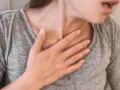 Kobieta z ręką na klatce piersiowej, odczuwająca duszności. To może być objaw po chorobie, wskazujący na potrzebę badań po covidzie.