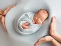 Otulony w błękitny kocyk śpi noworodek. Dookoła czuwają dłonie rodziców, tworząc bezpieczne gniazdko dla dziecka po 30. tygodniu ciąży.