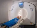 Pacjentka leży na stole tomografu komputerowego, przygotowana do badania. Widok pokazuje, jak wygląda tomografia komputerowa w praktyce.