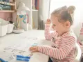Dziewczynka uczy się alfabetu na pamięć, kolorując litery. Zabawne obrazki pomagają w nauce.