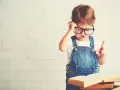 Mała uczona w okularach, z książkami, zastanawia się, jak nauczyć dziecko czytać 7 latka.
