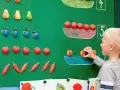 Chłopiec układa owoce na tablicy, ucząc się matematyki dla przedszkolaka. Kolorowe owoce pomagają w nauce liczenia.