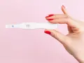Dłoń z czerwonymi paznokciami trzyma test ciążowy z dwoma kreskami. Co może zafałszować wynik testu ciążowego?