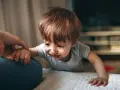 Małe dziecko płacze, trzymając się ręki rodzica. To moment, gdy pojawia się lęk separacyjny.