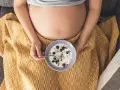 Ciężarna kobieta je jogurt z jagodami i granolą. Zdrowa przekąska w ciąży.