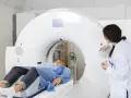 Pacjentka leży na stole tomografu, przygotowanie do tomografii z kontrastem. Lekarka obsługuje konsolę.