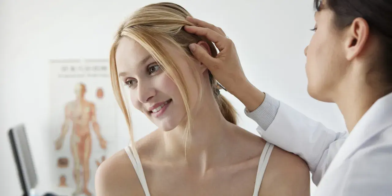Dermatolog bada skórę głowy pacjentki, delikatnie dotykając jej włosów.