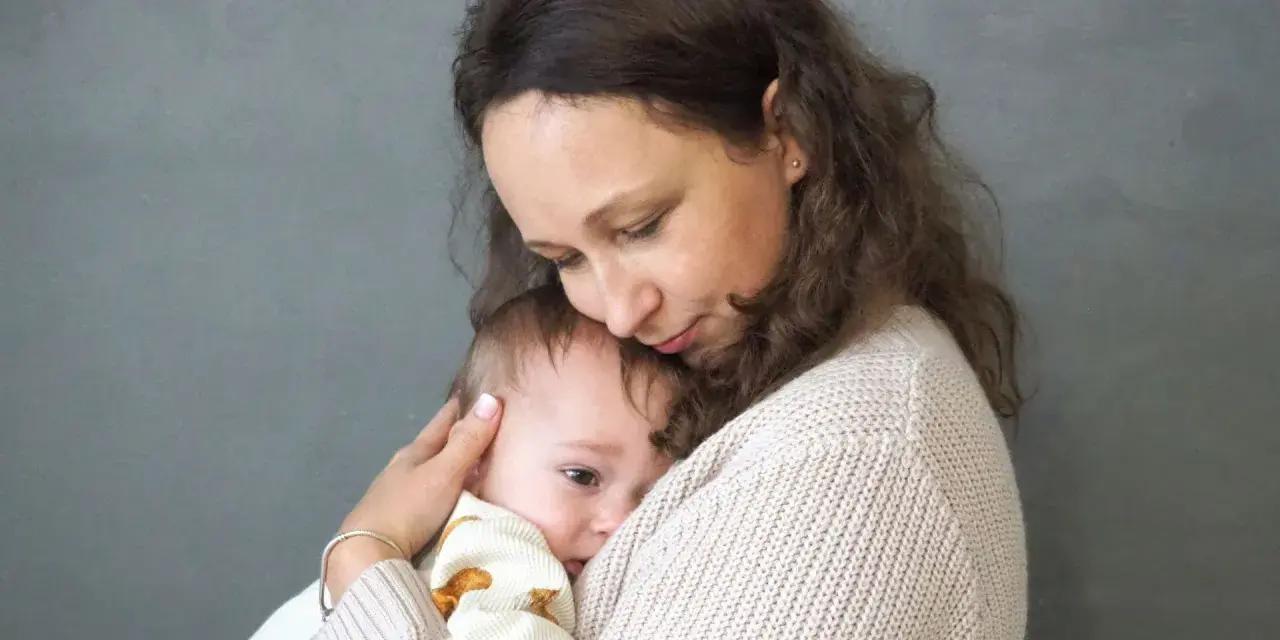 Mama tuli tulą do siebie dziecko, łagodząc lęk separacyjny u niemowlaka.