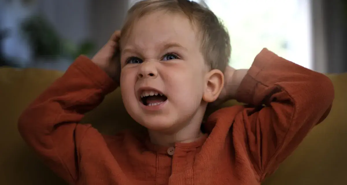 Mały chłopiec z wykrzywioną miną, trzymający się za głowę. Widać, że 10 latek nie radzi sobie z emocjami.