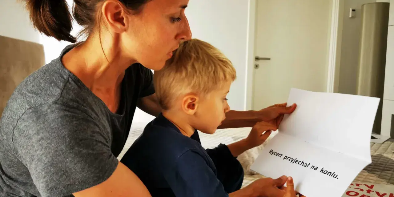 Mama pomaga synkowi czytać zdanie "Rycerz przyjechał na koniu". To świetny sposób, jak nauczyć dziecko szybko czytać.
