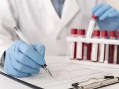 Laborant w rękawiczkach zapisuje dane pacjenta, obok stoją probówki z krwią do analizy CRP.