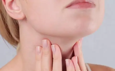 Kobieta dotyka szyi, gdzie znajduje się tarczyca. Wyniki badań wskazują na ft3 podwyższone tsh w normie, co może wymagać dalszej diagnostyki.
