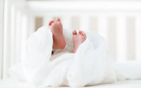 Małe stópki noworodka owinięte w biały kocyk. Wkrótce rodzice będą starać się dowiedzieć, kto wydaje akt urodzenia.