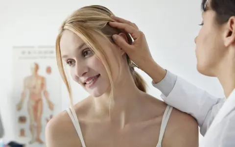 Dermatolog bada skórę głowy pacjentki, delikatnie dotykając jej włosów.