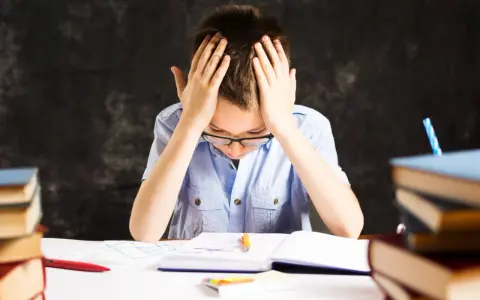 Chłopiec z rękami na głowie, otoczony książkami, zmaga się z nauką. Czy to dysleksja, co to za trudność?
