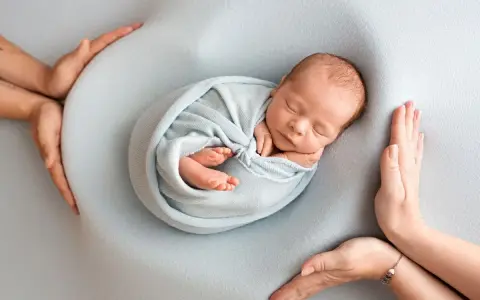Otulony w błękitny kocyk śpi noworodek. Dookoła czuwają dłonie rodziców, tworząc bezpieczne gniazdko dla dziecka po 30. tygodniu ciąży.