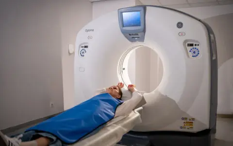 Pacjentka leży na stole tomografu komputerowego, przygotowana do badania. Widok pokazuje, jak wygląda tomografia komputerowa w praktyce.