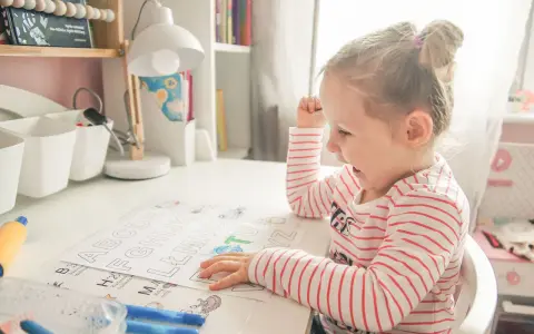 Dziewczynka uczy się alfabetu na pamięć, kolorując litery. Zabawne obrazki pomagają w nauce.