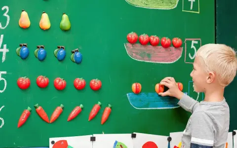 Chłopiec układa owoce na tablicy, ucząc się matematyki dla przedszkolaka. Kolorowe owoce pomagają w nauce liczenia.