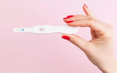 Dłoń z czerwonymi paznokciami trzyma test ciążowy z dwoma kreskami. Co może zafałszować wynik testu ciążowego?