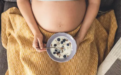 Ciężarna kobieta je jogurt z jagodami i granolą. Zdrowa przekąska w ciąży.