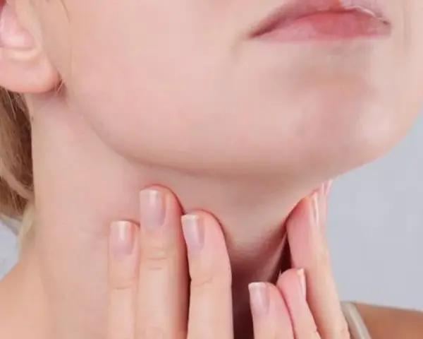 Kobieta dotyka szyi, gdzie znajduje się tarczyca. Wyniki badań wskazują na ft3 podwyższone tsh w normie, co może wymagać dalszej diagnostyki.