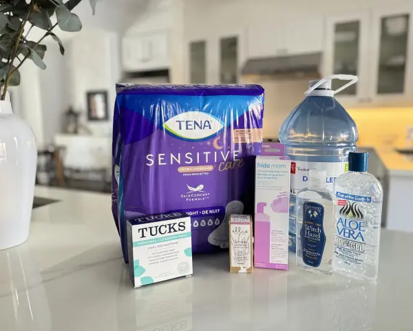 Zestaw produktów poporodowych: podpaski Tena, chusteczki Tucks, pianka do gojenia krocza Frida Mom, woda oczarowa i żel aloesowy.