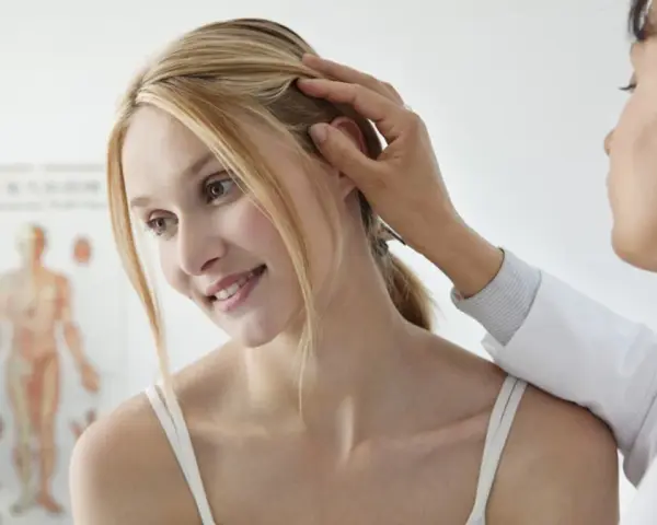 Dermatolog bada skórę głowy pacjentki, delikatnie dotykając jej włosów.