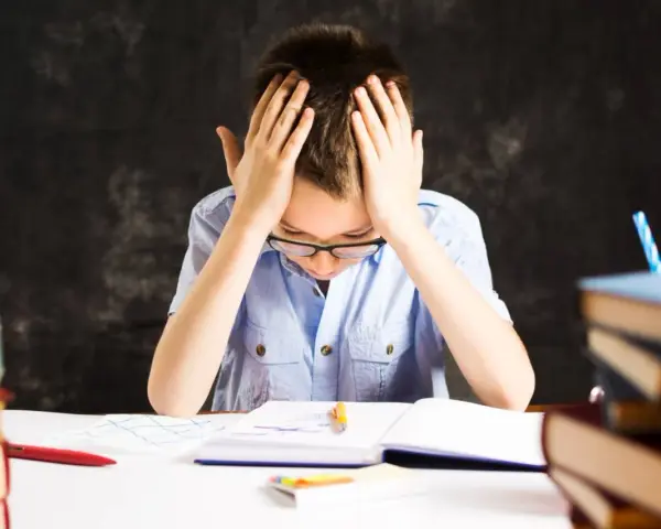 Chłopiec z rękami na głowie, otoczony książkami, zmaga się z nauką. Czy to dysleksja, co to za trudność?