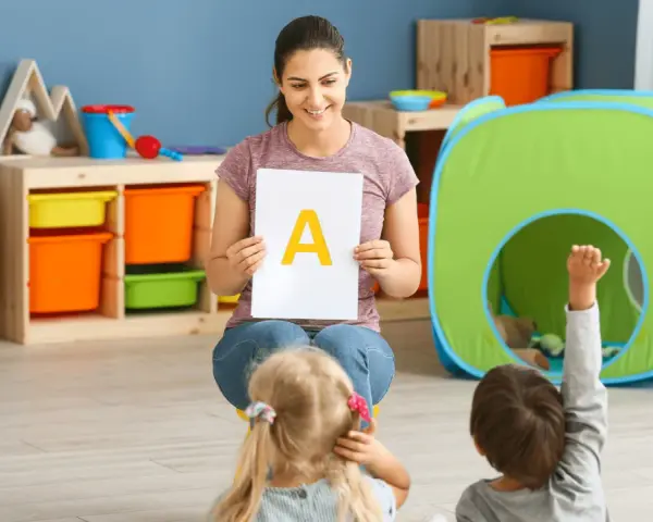 Nauczycielka prezentuje literę "A" dzieciom, stosując metodykę wprowadzania litery w przedszkolu. Jedno z dzieci podnosi rękę.