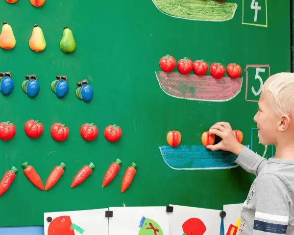 Chłopiec układa owoce na tablicy, ucząc się matematyki dla przedszkolaka. Kolorowe owoce pomagają w nauce liczenia.