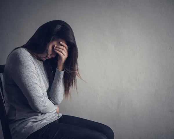 Kobieta zamyślona, z ręką na czole. Obraz symbolizuje trudności w zrozumieniu, jak wspierać osobę z depresją na odległość.