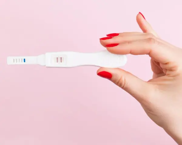 Dłoń z czerwonymi paznokciami trzyma test ciążowy z dwoma kreskami. Co może zafałszować wynik testu ciążowego?