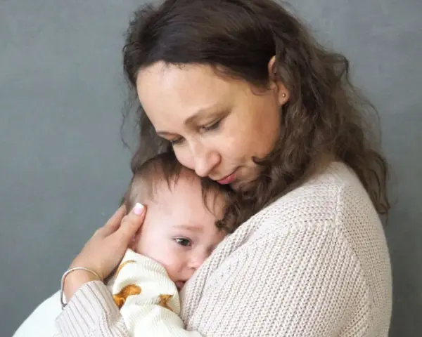 Mama tuli tulą do siebie dziecko, łagodząc lęk separacyjny u niemowlaka.