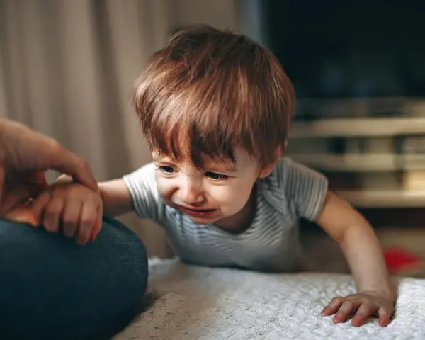 Małe dziecko płacze, trzymając się ręki rodzica. To moment, gdy pojawia się lęk separacyjny.