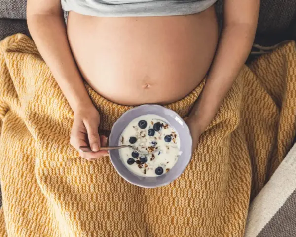 Ciężarna kobieta je jogurt z jagodami i granolą. Zdrowa przekąska w ciąży.