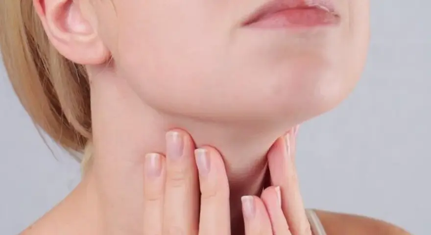 Kobieta dotyka szyi, gdzie znajduje się tarczyca. Wyniki badań wskazują na ft3 podwyższone tsh w normie, co może wymagać dalszej diagnostyki.