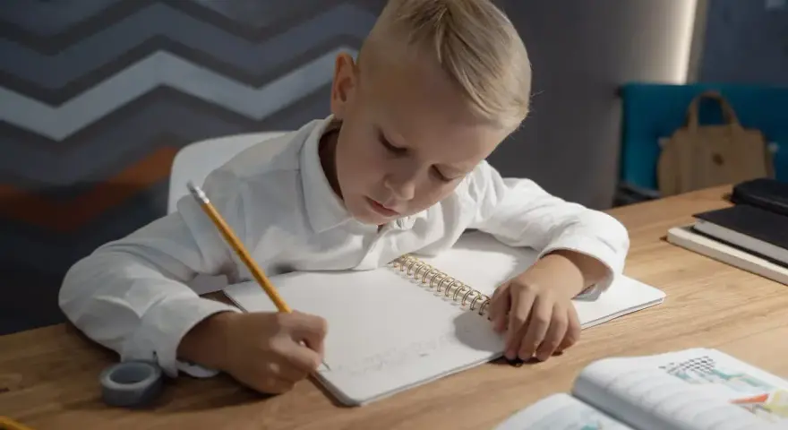 Chłopiec pisze w zeszycie, ćwicząc jak wytłumaczyć dziecku dodawanie i odejmowanie do 20.