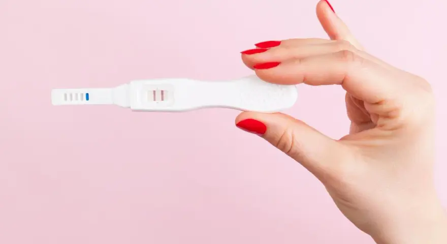 Dłoń z czerwonymi paznokciami trzyma test ciążowy z dwoma kreskami. Co może zafałszować wynik testu ciążowego?