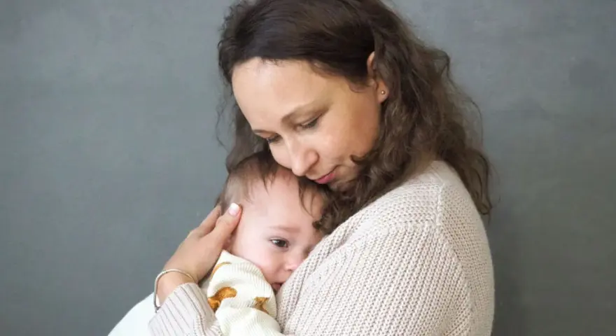 Mama tuli tulą do siebie dziecko, łagodząc lęk separacyjny u niemowlaka.