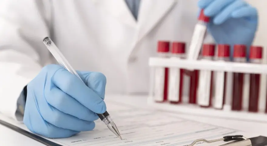 Laborant w rękawiczkach zapisuje dane pacjenta, obok stoją probówki z krwią do analizy CRP.