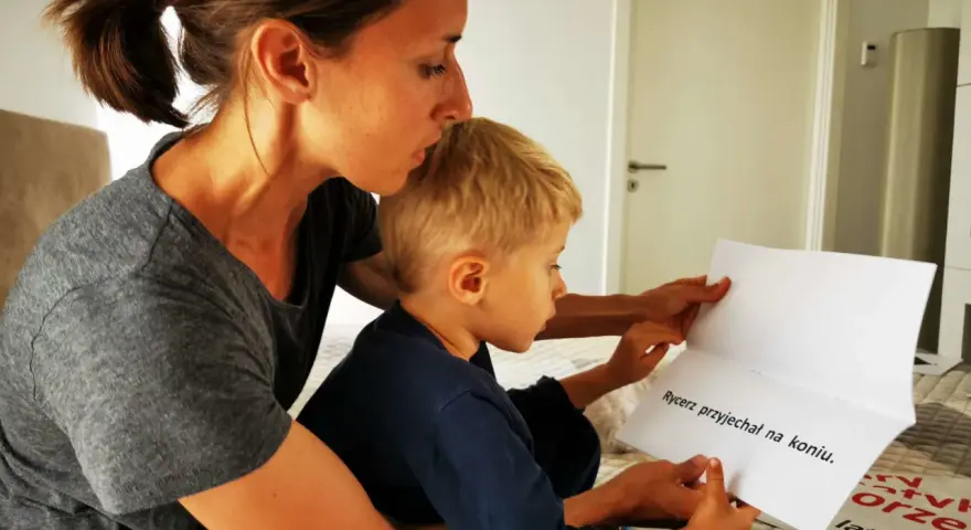 Mama pomaga synkowi czytać zdanie "Rycerz przyjechał na koniu". To świetny sposób, jak nauczyć dziecko szybko czytać.