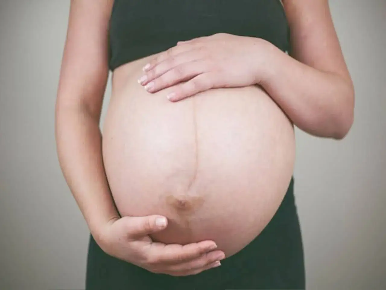 Brzuch ciężarnej kobiety, czułe dłonie obejmujące go, czuć, kiedy dziecko kopie.