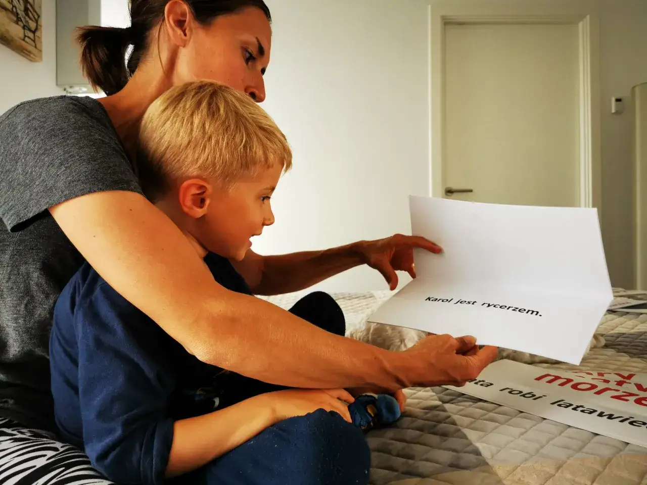Mama czyta synkowi książki dla 7-latka do samodzielnego czytania. Na kartce widnieje napis 
