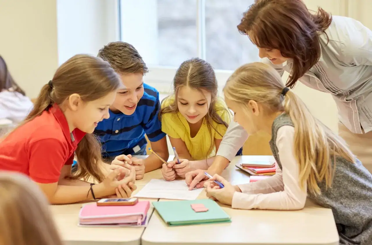 Nauczycielka pomaga grupie dzieci w zadaniu. Dzieci pracują razem, dyskutując o tym, czy dysleksja to niepełnosprawność.