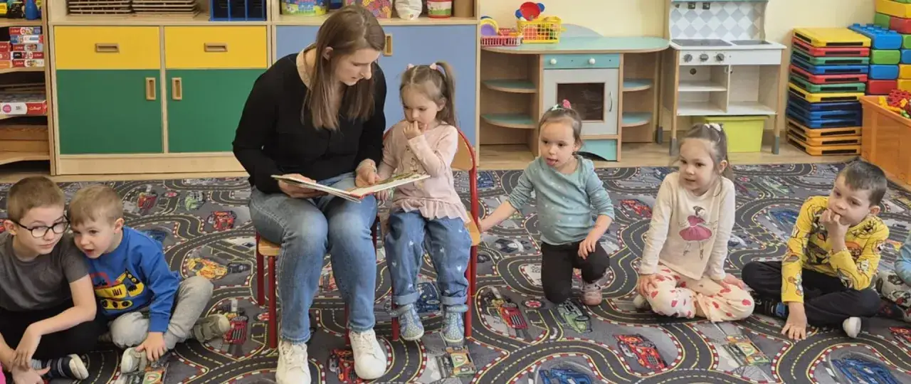 Nauczycielka czyta dzieciom w 2 klasie. Wszyscy słuchają uważnie, jak powinno czytać dziecko w 2 klasie.