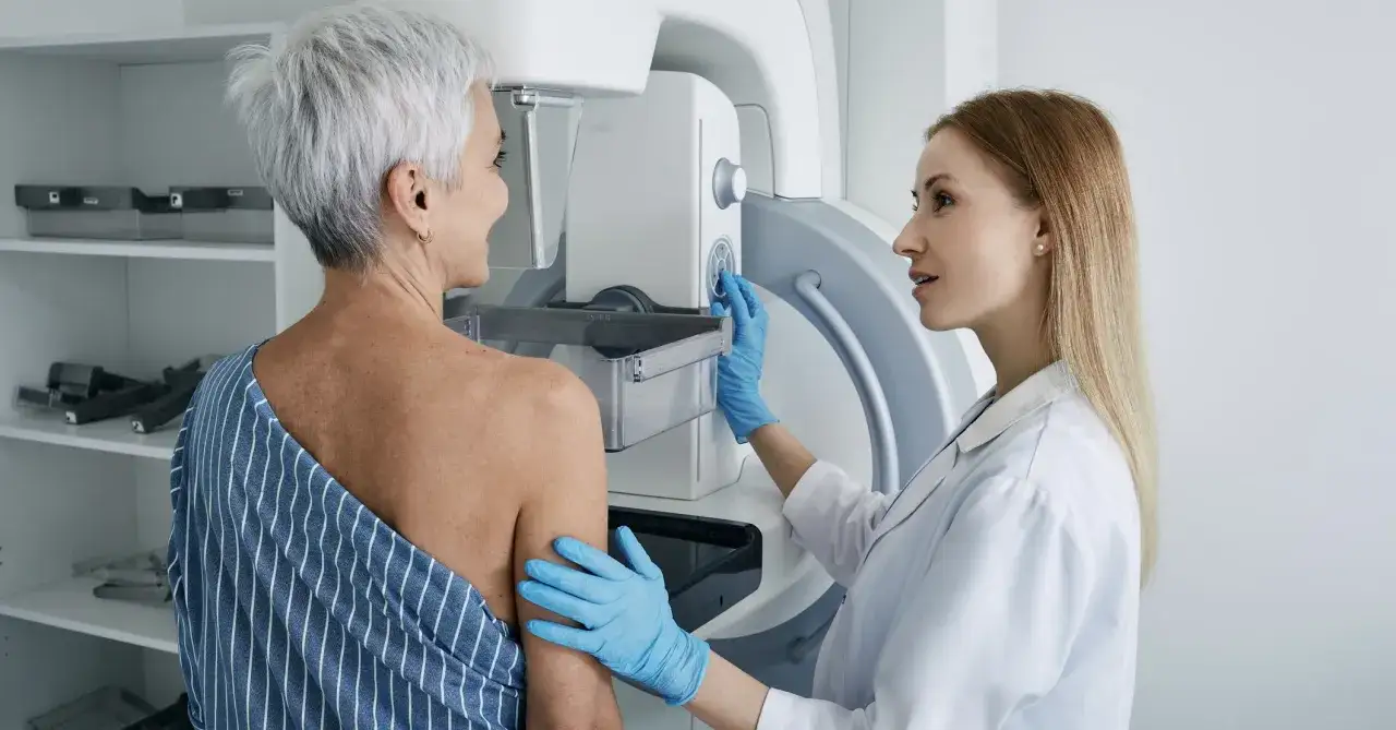 Pacjentka przygotowuje się do badania mammograficznego. Lekarka w rękawiczkach wyjaśnia, jak wygląda mammografia, delikatnie przykładając pierś do aparatu.