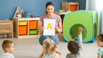 Nauczycielka prezentuje literę "A" dzieciom, stosując metodykę wprowadzania litery w przedszkolu. Jedno z dzieci podnosi rękę.